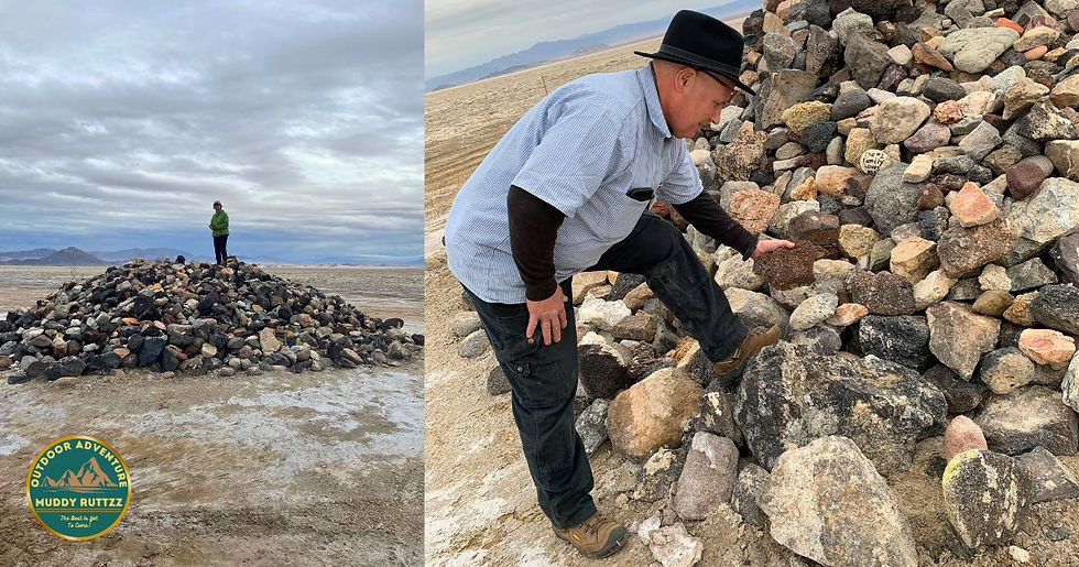 Man on a rock pile in a desert, wearing a black hat, examines stones. Another person in green stands on a rock mound under cloudy skies.