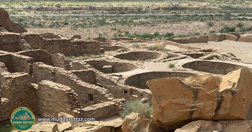 Ancient stone ruins with kivas in a desert landscape. The foreground shows large boulders. Text: "www.muddyrutzzz.com".