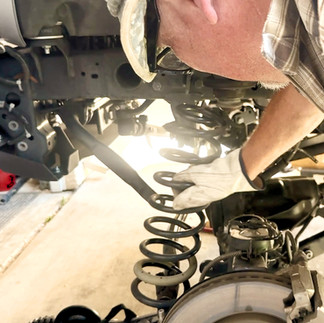 Jeep Gladiator front driver side tire removed and stock coil spring being removed.