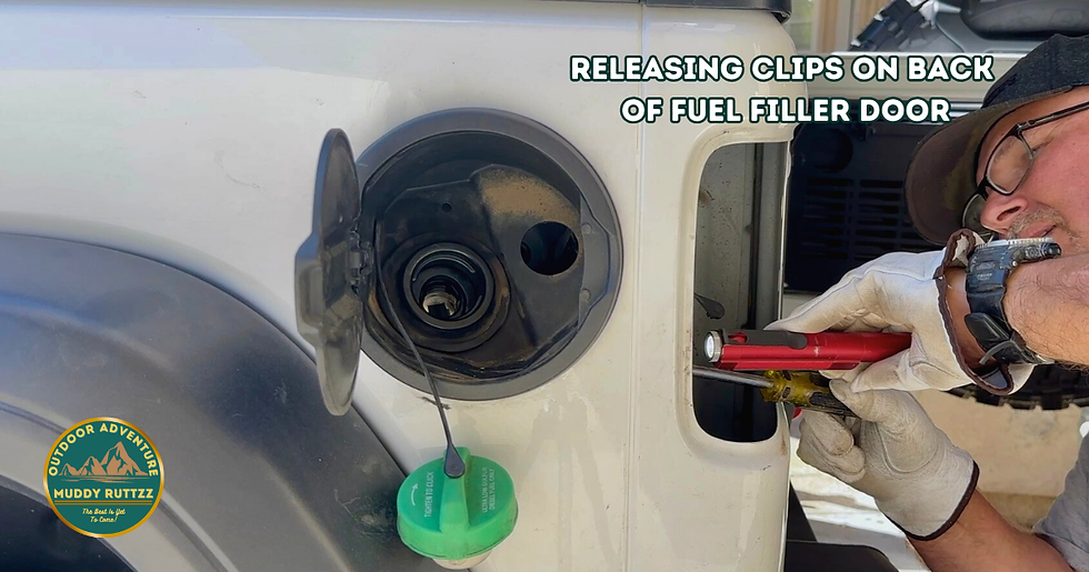 Fuel filler door of Jeep Wrangler Ecodiesel is open and green cap is hanging down. Tail light has been removed and man is using screwdriver to release tabs to remove fuel filler door.