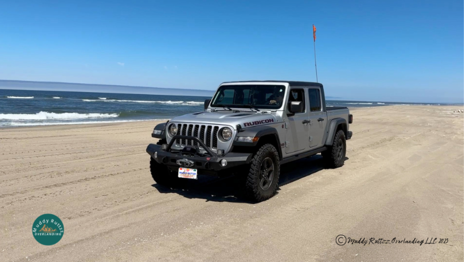 Silver Jeep Gladiator Rubicon Ecodiesel on Oregon Dunes Beach with sand flag mounted to back of vehicle.