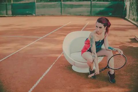 Weißer Tennis Sessel volley im Tennisball Design auf dem Tennisplatz, eine Person sitzt entspannt mit Tennisschläger darin, Tennis Möbel von lillus