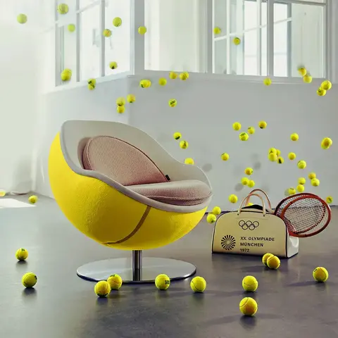 Tennis Sessel volley steht in einer Squashhalle in Seitenansicht, daneben eine Tennistasche mit Tennisschläger und mehrere Tennisbälle auf dem Boden von lillus