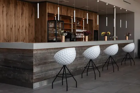 Four Eagle bar stools in a white golf ball design stand in front of a counter in the golf club, manufacturer lillus