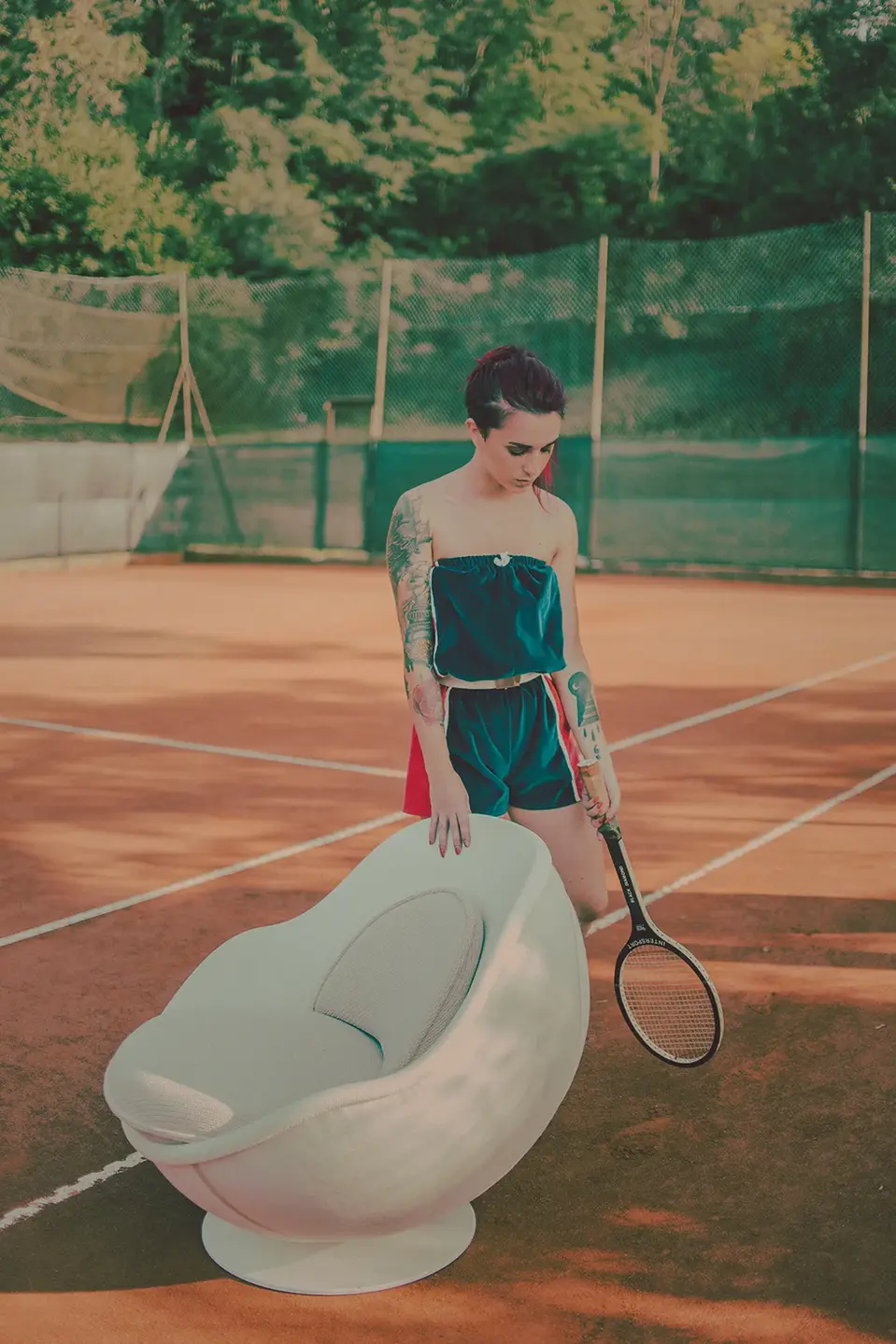 Weißer Tennis Sessel volley im Tennisball Design in Seitenansicht auf dem Tennisplatz, daneben steht eine Person, Tennis Möbel von lillus