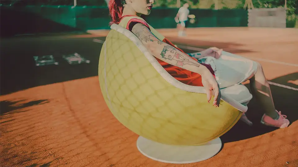 Tennis Sessel volley steht am Seitenrand eines Tennisplatzes, eine Person sitzt entspannt darin und verfolgt das Tennisspiel von der Seite von lillus