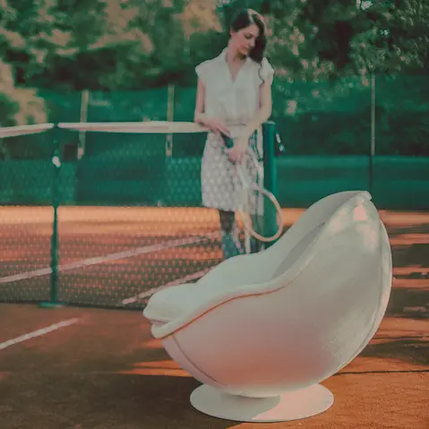 Weißer Tennis Sessel volley auf einem Tennisplatz, im Hintergrund eine Person mit Tennisschläger am Netz von lillus