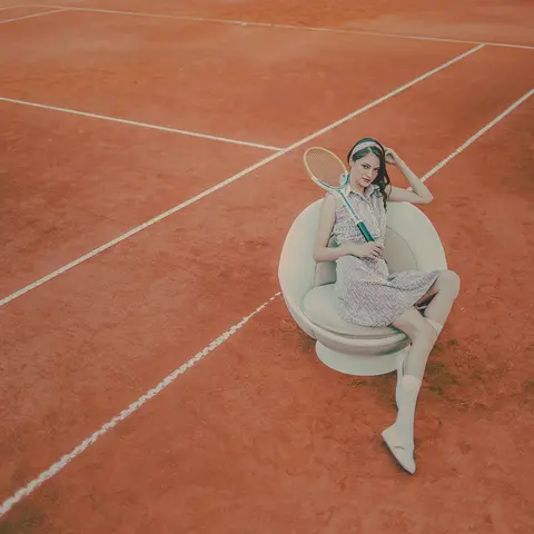Weißer Tennis Sessel volley auf dem Tennisplatz aus erhöhter Perspektive, eine Person mit Tennisschläger sitzt entspannt darin auf dem Spielfeld von lillus