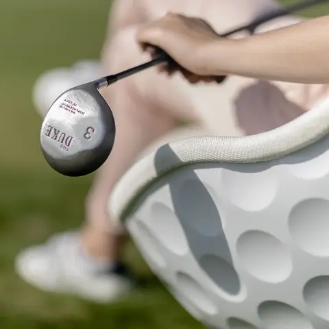 Focus on the dimples and the white ABS plastic of an Eagle lounge chair with golf clubs, manufacturer Lillus.