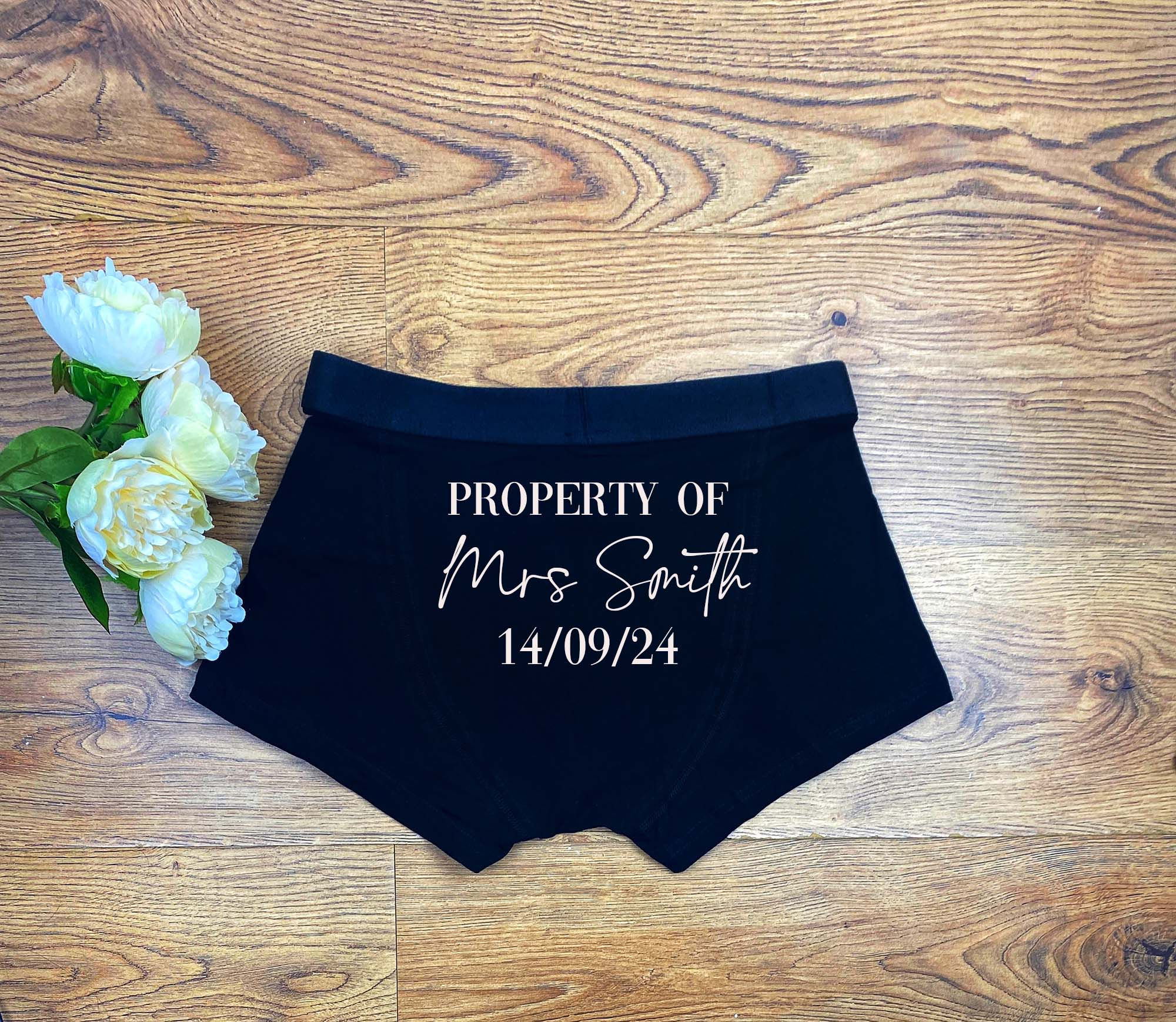 Black boxers trunks for men with a white text on the back side Property of Mrs Smith 15/09/22.
