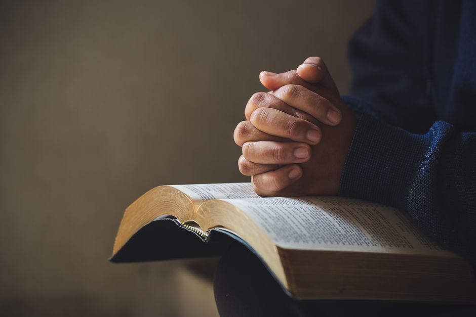 A pair of folded hands dramatically resting over an open bible