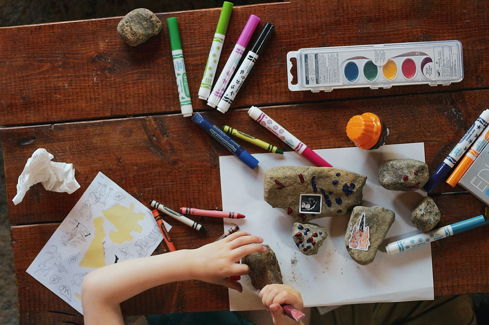 A child coloring rocks on a wood table.