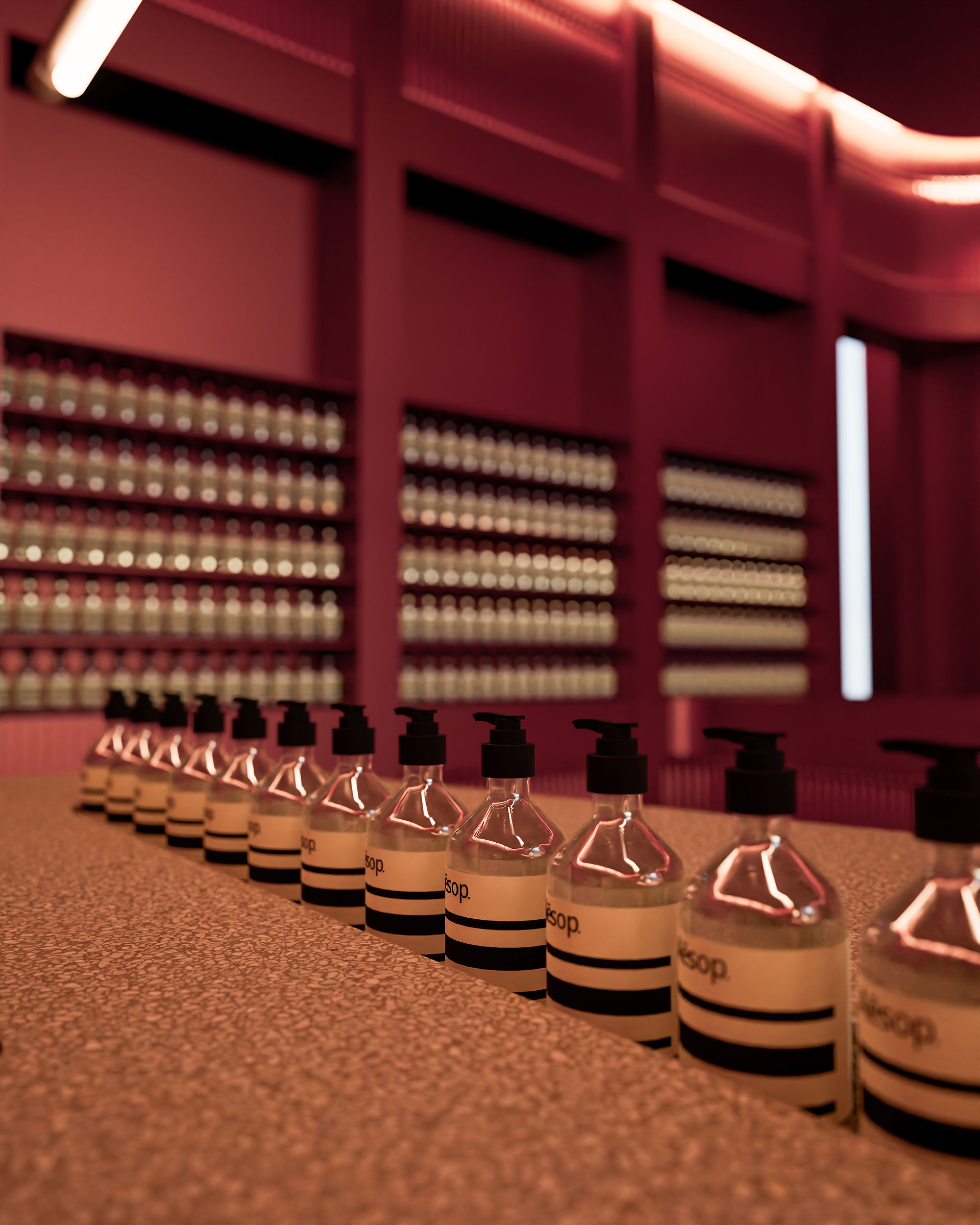 Close-up retail interior visualization of pump bottles on a textured counter with warm burgundy lighting and softly blurred product shelves.