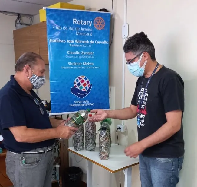 Dois homens rotarianos, observando algumas garrafas de refrigerantes preenchidas com lacres de alumínio