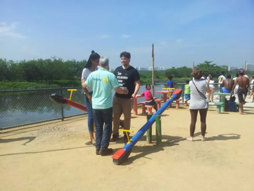 àrea aberta de praça com gangorra , ao lado rotarianos conversando e ao fundo crianças brincando