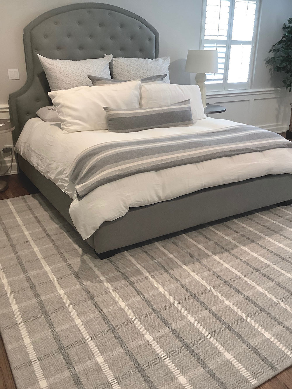 Bedroom with gray tufted bed and plaid rug