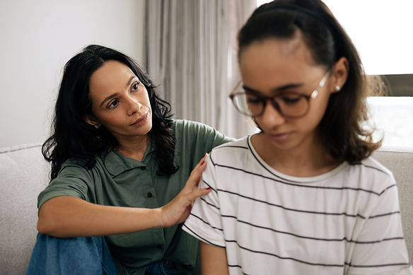 Caring mother comforting her teenage daughter, both sitting on the couch at home, sharing