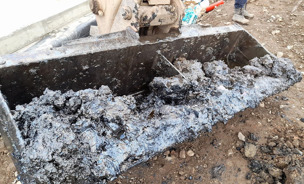 An excavator bucket full of made ground so heavily contaminated with hydrocarbons it's black and sloppy with an oily sheen