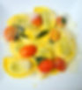 Ein Teller mit Ravioli, serviert mit gelber Sauce, Kirschtomaten, frischem Salbei und reichlich geriebenem Parmesan, angerichtet auf einem weißen Teller.
