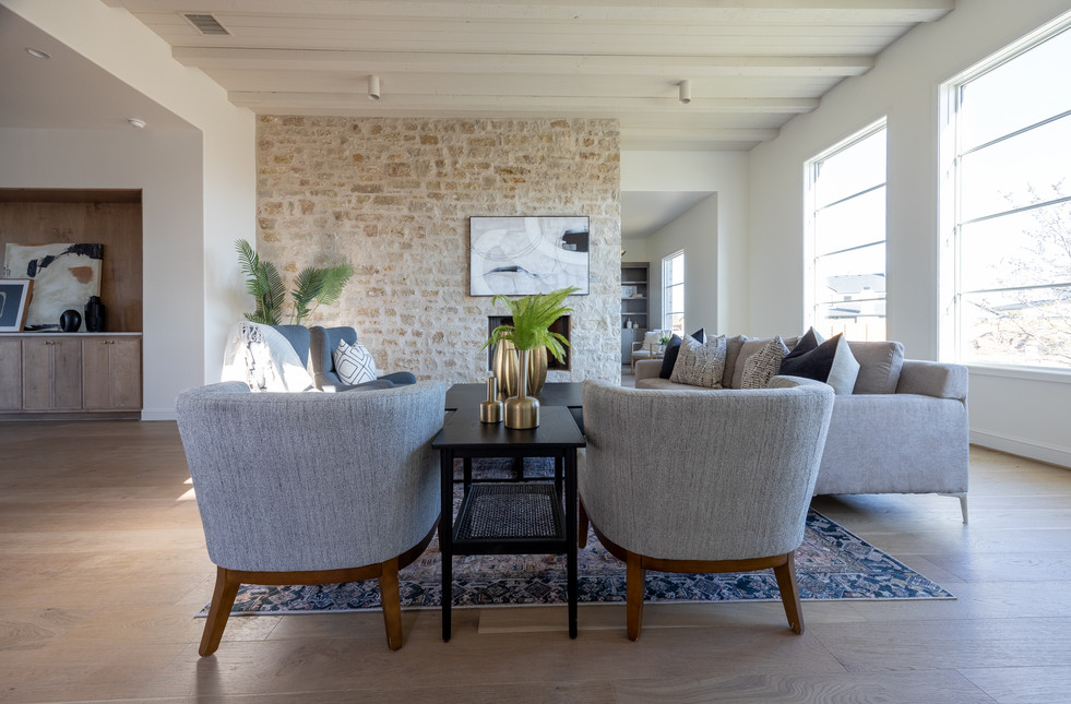 Spacious living room with gray sofas, stone fireplace, abstract art, and wooden dining set. Natural light from large windows; modern decor.