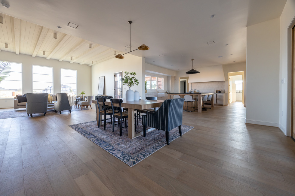 Spacious living room with gray sofas, stone fireplace, abstract art, and wooden dining set. Natural light from large windows; modern decor.