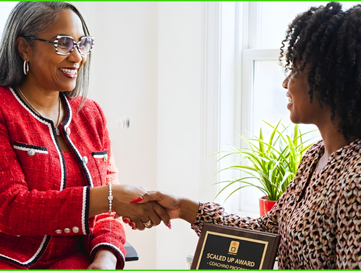 Two women shaking hands; one in a red suit, the other holding a plaque reading "Scaled Up Award." They're smiling in a bright office.