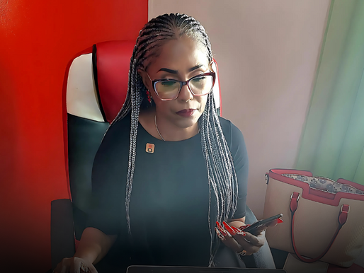 Woman with braided hair focuses on her phone at a desk. She sits in a red and black chair against a red wall, with a red and white bag nearby.