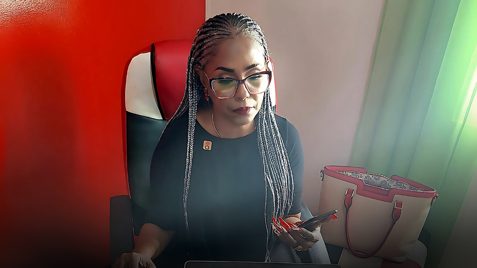 Woman with braids, in black, using phone at desk. Red and black chair, bag nearby. Red wall, green curtain in background. Focused mood.