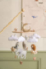 A close up image of a safari-inspired mobile, with felt zebra, lion, elephant and giraffe, hanging above a crib.