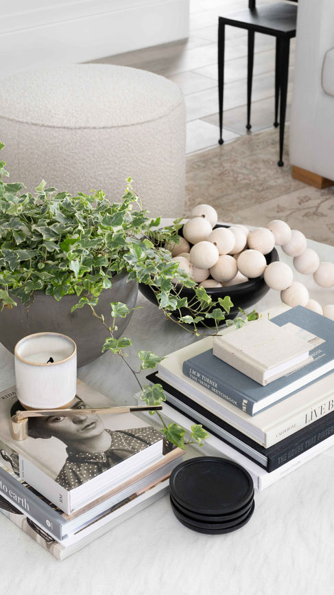 Marble coffee table styled with stacks of books, a candle, wooden beads, decor and a plant, by Miami interior designers The Habitat Collective