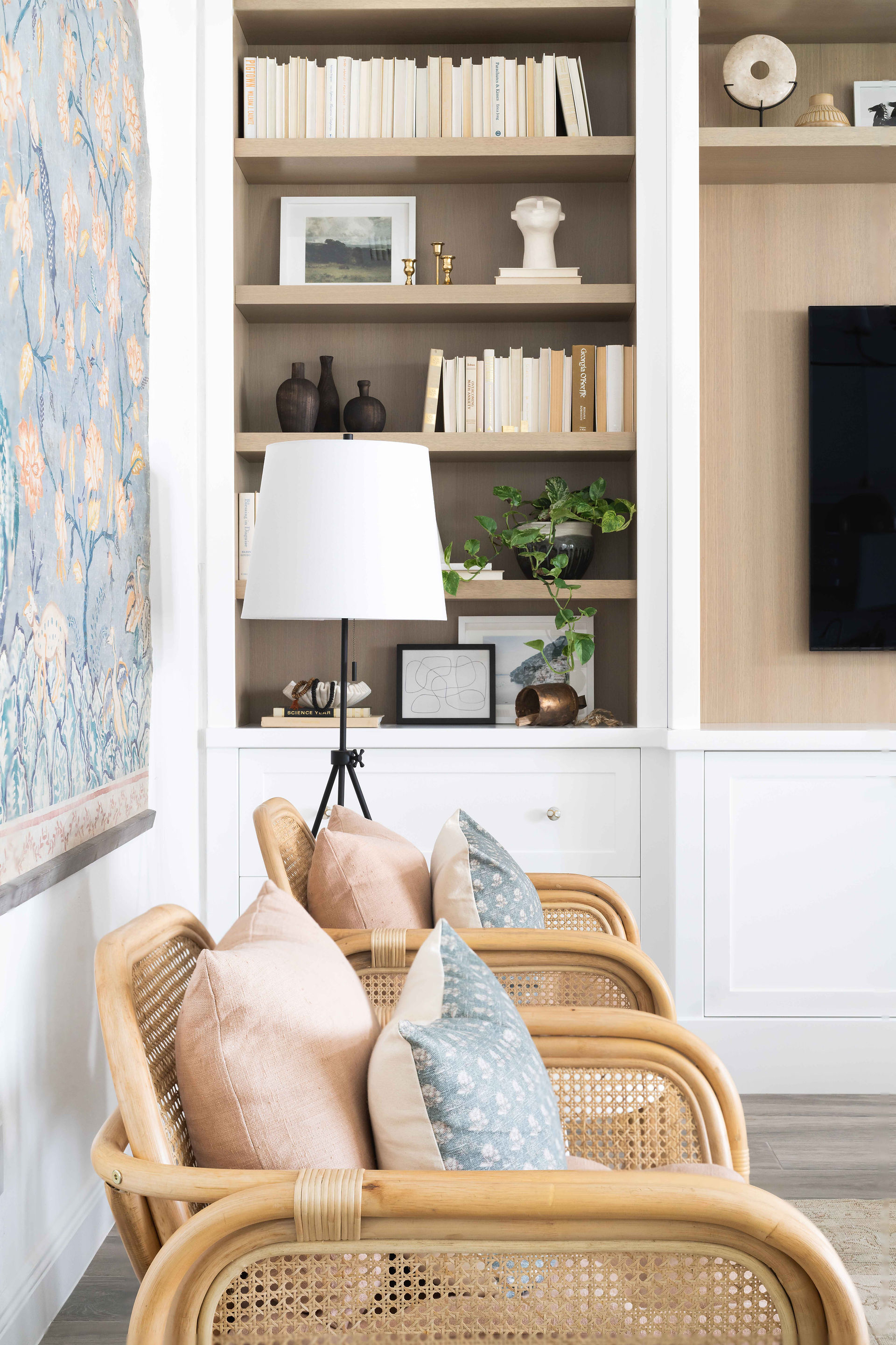 Cane chairs in front of a white and wood built in, shelves styled with books and decor, designed by Miami interior designers The Habitat Collective