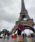 Woman with umbrella stands before the Eiffel Tower in Paris France.