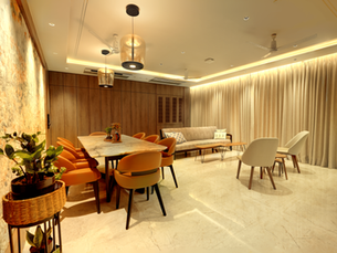 Modern dining room with orange chairs, marble table, sofa, curtains, and ceiling fans under warm lighting