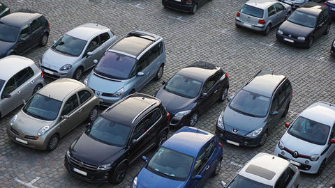 Parking pavé vu d’en haut, voitures compactes garées serrées, tons gris, noir et bleu, ambiance calme.