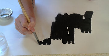 Photograph of a hand wielding a paintbrush and painting a large black castle.