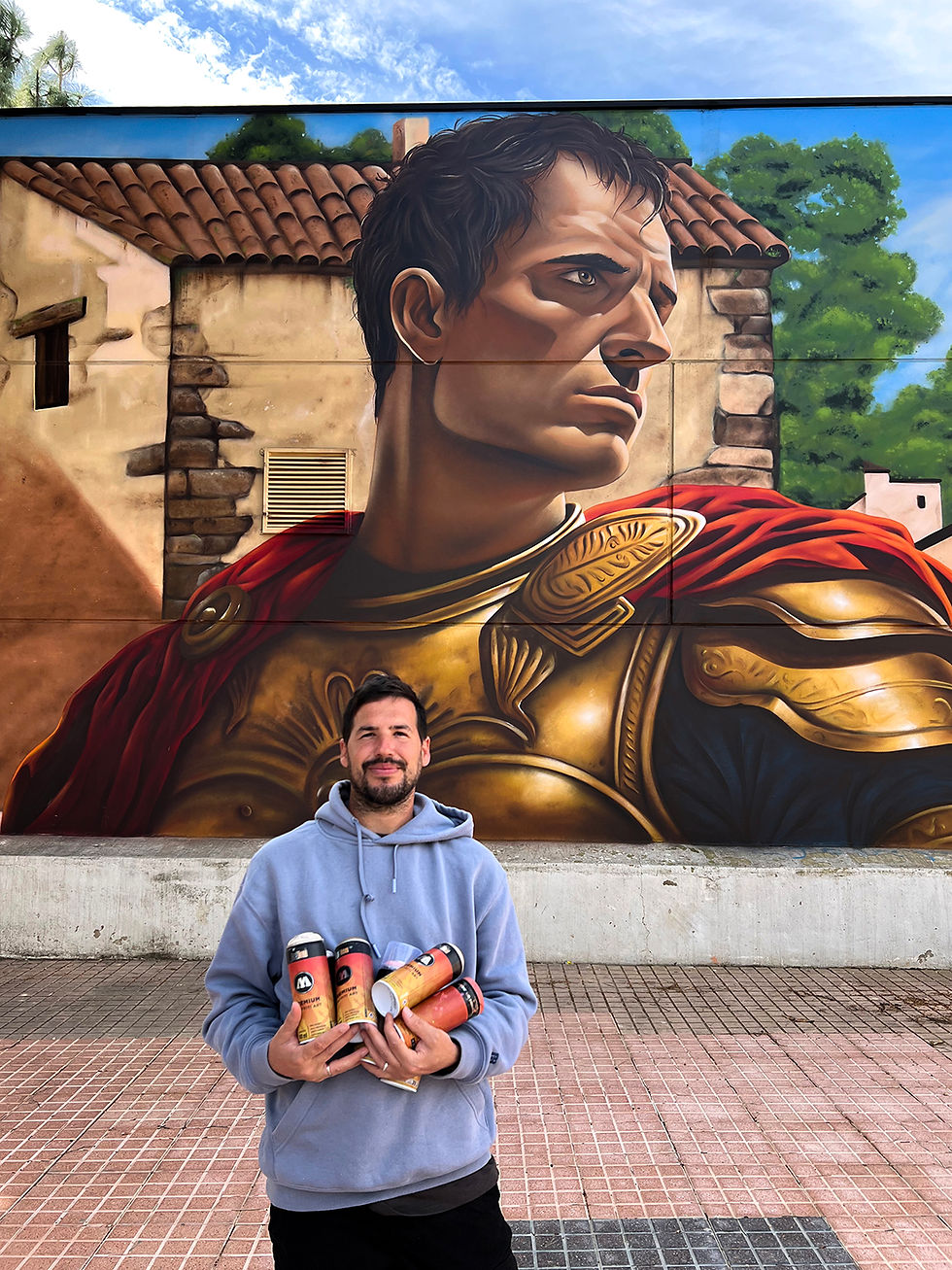El artista Kato junto el mural sosteniendo varios sprays.