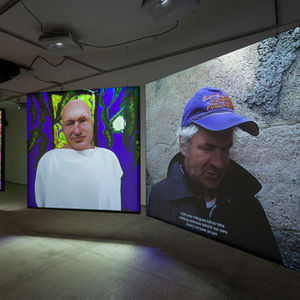 Installation view of Seen with multiple screens showing listening avatars and a live performer reading poetry