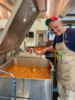Smiling man stirring large stew pot; "Food Bank of Nevada County" apron.