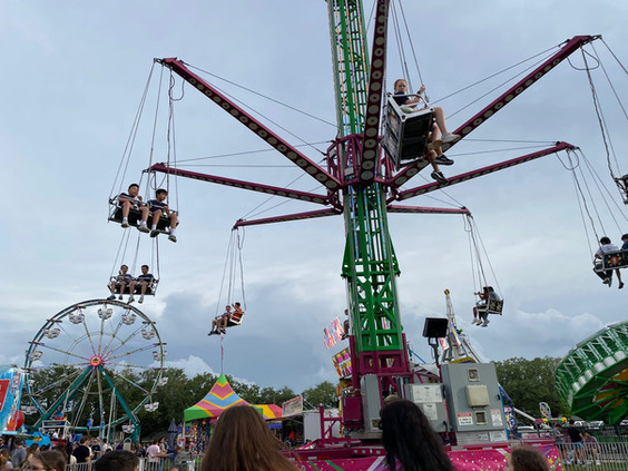 People enjoying a carnival swing ride with a Ferris wheel in the background.