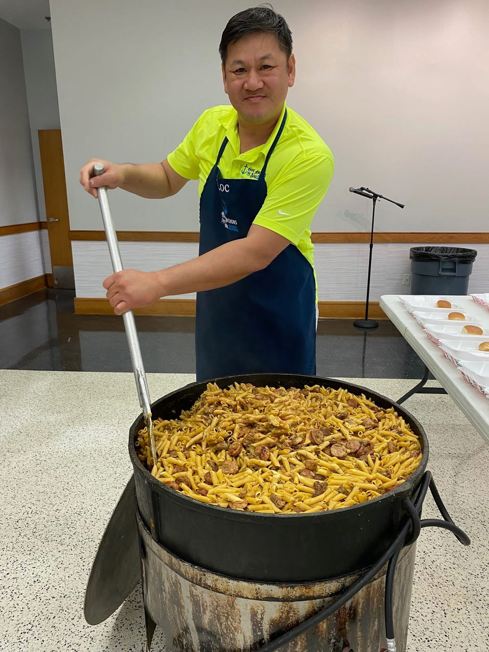 Man in apron stirs large pot of food at a community event.