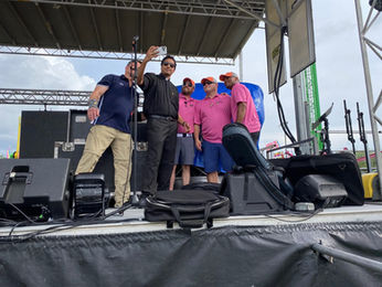 Priest taking a selfie with four men on an outdoor stage.
