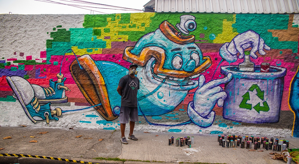 ArtistaPakato em frente ao seu painel (audiodescrição abaixo)