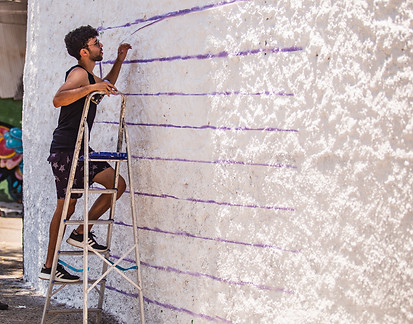 Artista dando os primeiros traços no muro para a criação do seu painel.