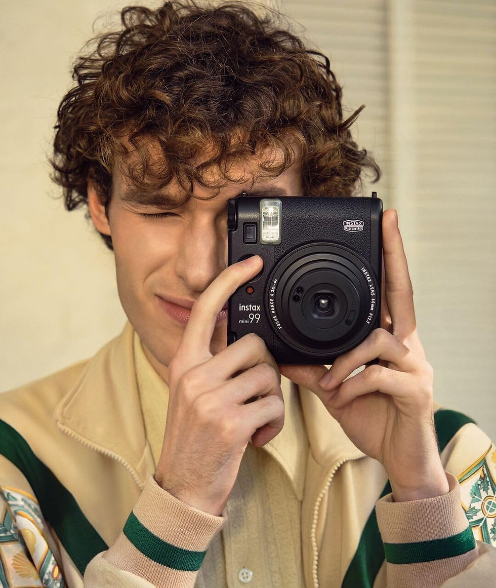Un homme aux cheveux bouclés tient un appareil photo Instax Mini 99.