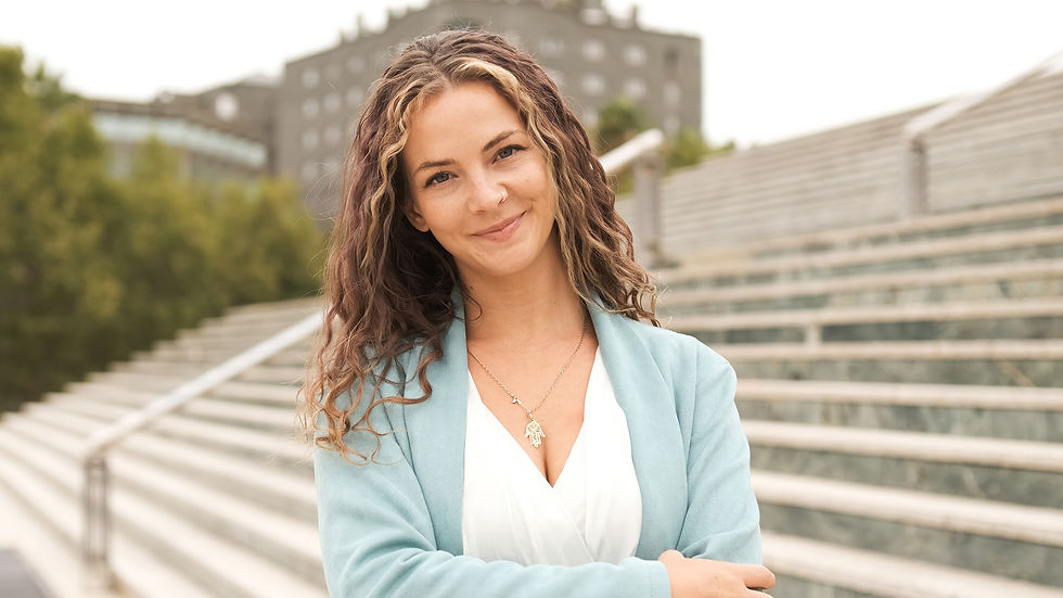 Femme souriante en tenue bleu clair et blanche, devant un escalier en extérieur.