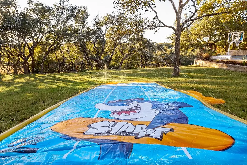 Spacious backyard with colorful kite, mature oak trees, and basketball hoop in Dripping Springs
