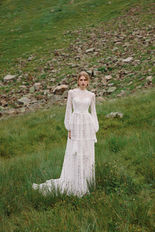 Model trägt weißes Brautkleid auf der Wiese, BRAUTKLEIDER, Boho, vor grüner Landschaft.
