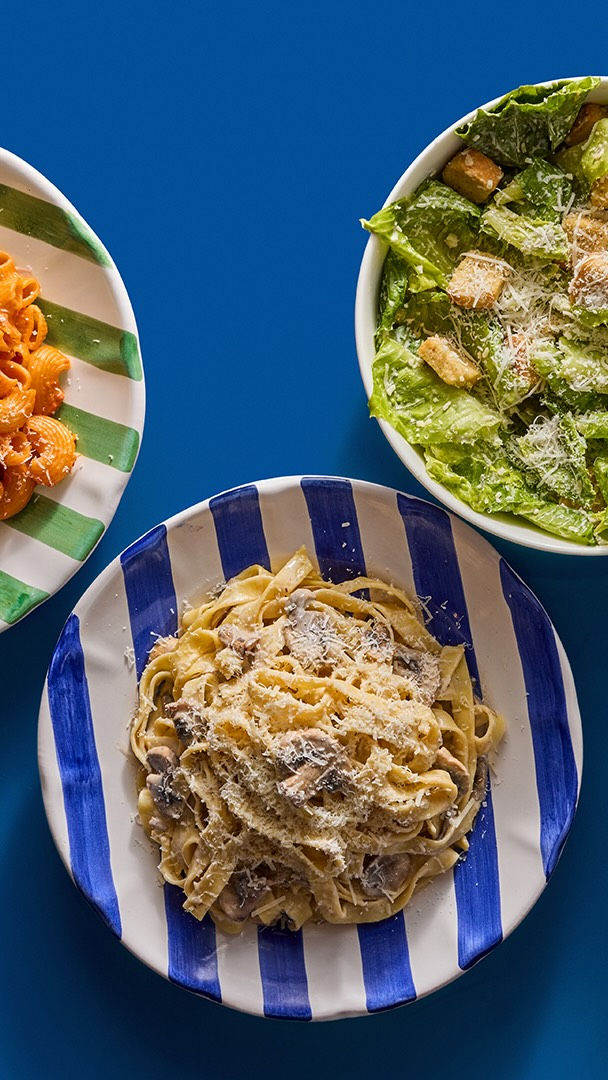 Food inspiration: a plate of creamy pasta alongside salad and another pasta dish on a blue table