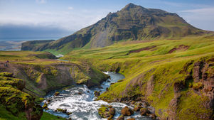 Green mountain valley with a river waterfall, mossy cliffs, and tiny hikers under a blue sky.