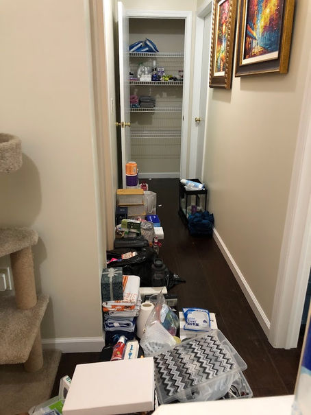A closet is being decluttered and organized, with one side of the hallway loosely organized with groups of items. Some items remain in the closet, a work in progress. 